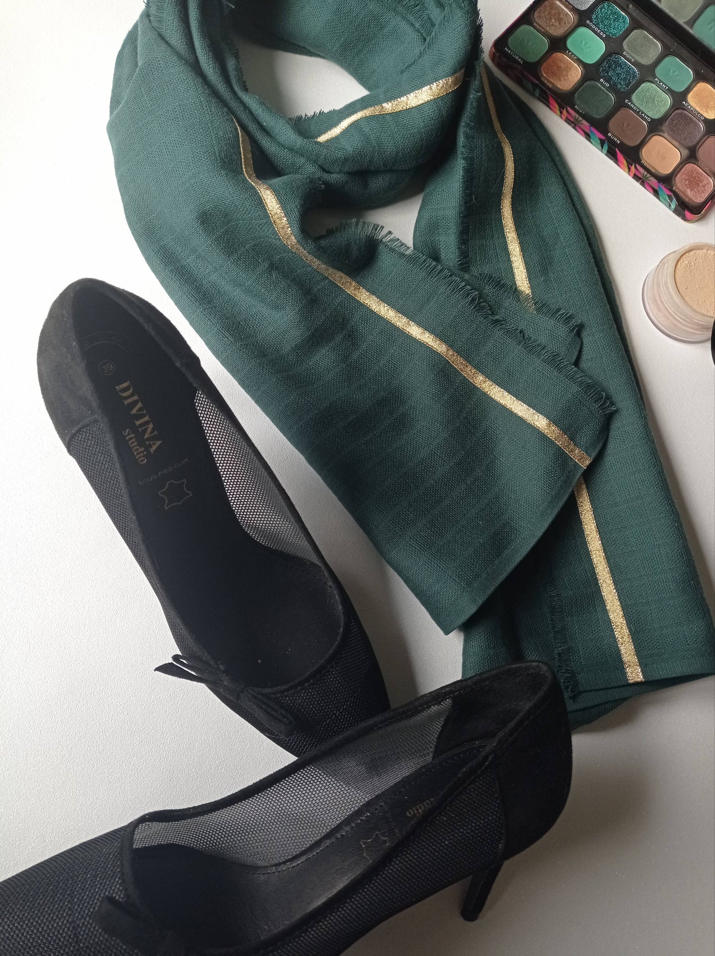 foulard vert ligne or entouré d'escarpin noir et d'une palette de maquillage